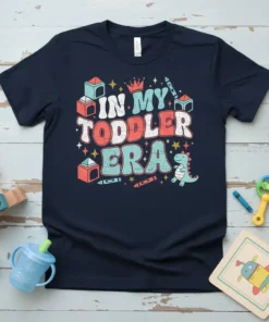 Retro "In My Toddler Era" text with a cute dinosaur and building blocks graphic on a navy t-shirt