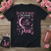 Black t-shirt with "In October We Wear Pink" text, a witch on a broom, moon, and pink ribbons