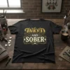 Black t-shirt with gold and cream text reading "INKED AND SOBER" in decorative vintage font, featuring a diamond graphic