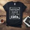 Black t-shirt with "Introverted but willing to discuss cats." text, featuring a sleeping cat graphic and paw prints