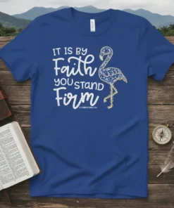 Blue t-shirt with white and gold text "IT IS BY Faith YOU STAND Firm" and a decorative flamingo graphic. Includes