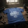 It Was Broken When I Got Here quote on a blue t-shirt, featuring distressed text and a gear graphic