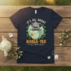 Cute koala peeking out of a teacup with "It's All About Koala-Tea" text, navy t-shirt design