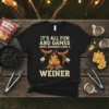 Black t-shirt with "IT'S ALL FUN AND GAMES UNTIL SOMEONE LOSES A WEINER" text, featuring hot dogs on forks over