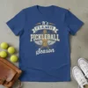 It's Always Pickleball Season text with pickleball graphics and wings on a blue t-shirt