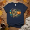 It's Fall Y'all text with a pumpkin and autumn leaves graphic on a navy t-shirt