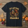 Thanksgiving t-shirt with "it's giving thanks" text and a colorful turkey graphic surrounded by autumn leaves and stars