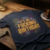 Navy t-shirt with "IT'S MY FUCKING BIRTHDAY" in large yellow text, surrounded by colorful fireworks and confetti