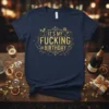 Navy blue t-shirt with gold glitter text reading "IT'S MY FUCKING BIRTHDAY" surrounded by party graphics like champagne glasses and