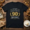 Black t-shirt with "IT'S MY GRANDMA'S 90TH BIRTHDAY" in gold and white glittery text, surrounded by laurel wreaths