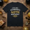 Black t-shirt with white and gold text reading "IT'S MY HUSBAND'S 40TH BIRTHDAY" and gear graphics