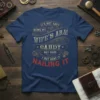 Navy blue t-shirt with vintage distressed text: "It's Not Easy Being My Wife's Arm Candy But Here I But Here