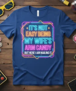 Neon sign style text "IT'S NOT EASY BEING MY WIFE'S ARM CANDY BUT HERE I AM NAILING IT" on a