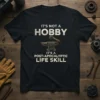 Black t-shirt with white text: "IT'S NOT A HOBBY IT'S A POST-APOCALYPTIC LIFE SKILL" featuring an anvil and hammer graphic