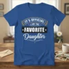 Blue t-shirt with "IT'S OFFICIAL I AM THE FAVORITE Daughter" text in a playful, bold font, laurel wreath accents