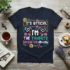 Navy blue t-shirt with "IT'S OFFICIAL I'M THE FAVORITE DAUGHTER-IN-LAW" text in colorful, playful fonts, surrounded by floral and heart