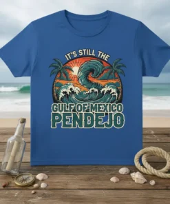 T-shirt with bold text "IT'S STILL THE GULF OF MEXICO PENDEJO" over a stylized wave and palm trees, vintage sunset