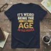 T-shirt with the text "IT'S WEIRD BEING THE SAME AGE AS OLD PEOPLE" in a distressed, retro font style