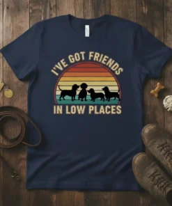 Dachshund silhouettes against a retro sunset with text "I've Got Friends In Low Places" on a navy t-shirt