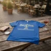 Blue t-shirt with "Joie De Vivre PARIS" text and an Eiffel Tower graphic, set on a wooden table outdoors