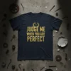 Navy t-shirt with gold glitter text "JUDGE ME WHEN YOU ARE PERFECT" and a laurel wreath graphic above the text