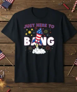 Black t-shirt with white text "JUST HERE TO BANG" and a red, white, and blue rocket launching with fireworks