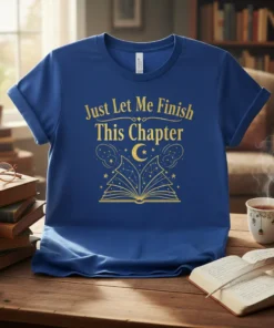 Blue t-shirt with gold text "Just Let Me Finish This Chapter" above an open book graphic with stars and constellations