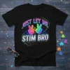 Black t-shirt with "JUST LET ME STIM BRO" text, colorful peace signs, and puzzle piece graphics