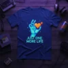 Pixel art design with text "JUST ONE MORE LIFE" and a hand holding a heart, on a navy blue t-shirt