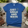 Blue t-shirt with "JUST SMILE AND WAVE" text and a hand waving graphic