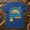 T-shirt design with text "JUST A BOY WHO LOVES DINOSAURS AND TRAINS" featuring cartoon dinosaurs and a train