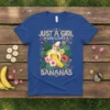 Just A Girl Who Loves Bananas text with a cute smiling banana graphic and tropical flowers on a blue t-shirt