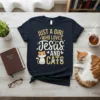 Graphic t-shirt with "Just A Girl Who Loves Jesus And Cats" text, featuring a cute cat illustration and religious symbols