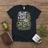 Just A Girl Who Loves JESUS and PICKLES text design with a cross and pickle graphic on a black t-shirt
