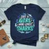 Navy t-shirt with "JUST A GIRL WHO LOVES SHARKS" text in teal and white, surrounded by shark graphics and hearts