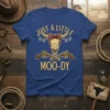 Just A Little Moo-dy text on a blue t-shirt with a cow skull wearing a bandana and crossed revolvers graphic