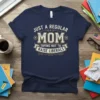 Navy t-shirt with "JUST A REGULAR MOM TRYING NOT TO RAISE LIBERALS" in distressed cream and gold vintage typography, featuring