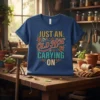 Funny "Just An Old Hoe Carying On" gardening quote t-shirt with floral and tool graphics on a blue tee