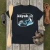 Black t-shirt with white text "kayak cat" above a graphic of a person kayaking down a river with a cat