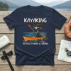 Black cat in kayak with paddle, text "KAYAKING BECAUSE MURDER IS WRONG" on navy t-shirt