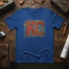 KC Blueprint Design T-Shirt featuring red 'KC' letters with gold blueprint background of city elements and gears