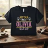 Black t-shirt with "KEEP CALM AND LET OLIVIA Handle That!" text and lion graphics, featuring pink glittery "OLIVIA"
