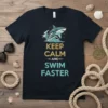 Keep Calm and Swim Faster quote with a shark jumping out of waves graphic on a navy t-shirt