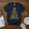 Keep Calm and Trust Your Health Inspector quote t-shirt with a laurel wreath graphic above the text in yellow distressed