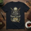 Keep Clam and Proof Read quote in decorative font on a navy t-shirt with clam, pearl, feathers, books, and magnifying