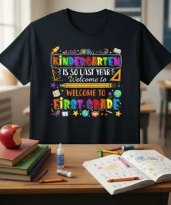 Black t-shirt with colorful "Kindergarten Is So Last Year Welcome To First Grade" text and school-themed graphics