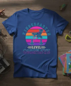 Kindergarten Level Complete t-shirt with retro rocket ship and game controllers, vibrant sunset background