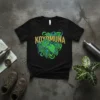 Black t-shirt with the word KOYOMUNA in gold glitter above a cluster of vibrant green philodendron leaves