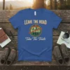 Leave The Road Take The Trails quote on a blue t-shirt with a circular mountain and trees graphic