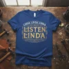 Blue t-shirt with gold text "Linda Linda Linda LISTEN LINDA" in decorative font, featuring gears and swirls
